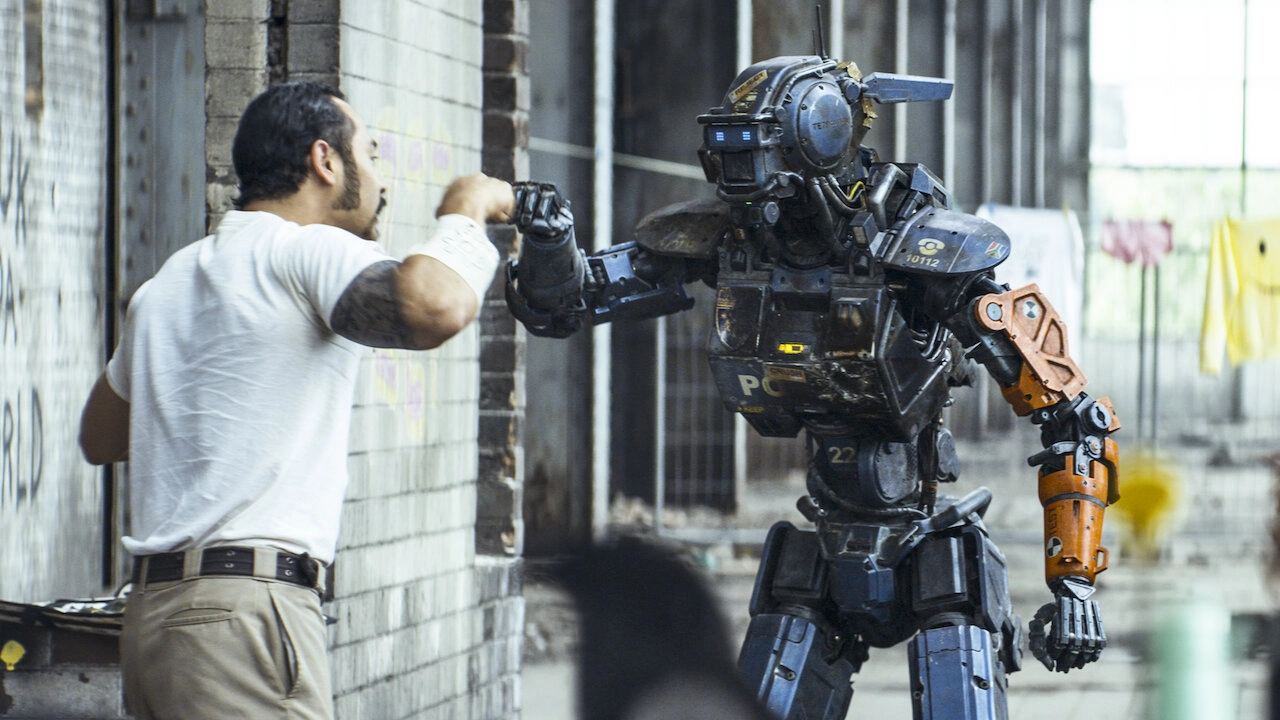 Man in a white shirt punches a large armored robot in a gritty alley.