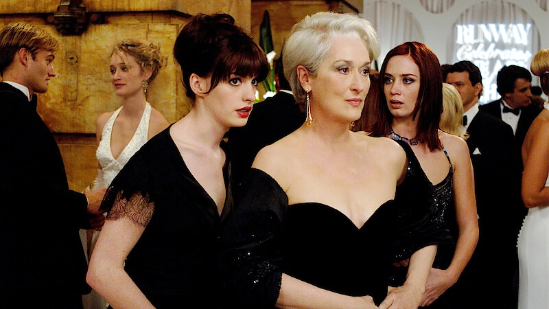 Three women in black evening gowns pose on the red carpet at a formal gala event. Note: avoid identifying individuals or exact names; describe scene and attire.