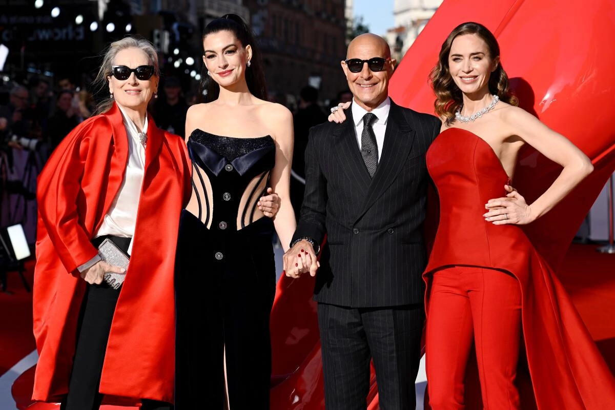 Four celebrities pose on a red carpet in stylish evening wear, smiling for cameras with a red backdrop behind them