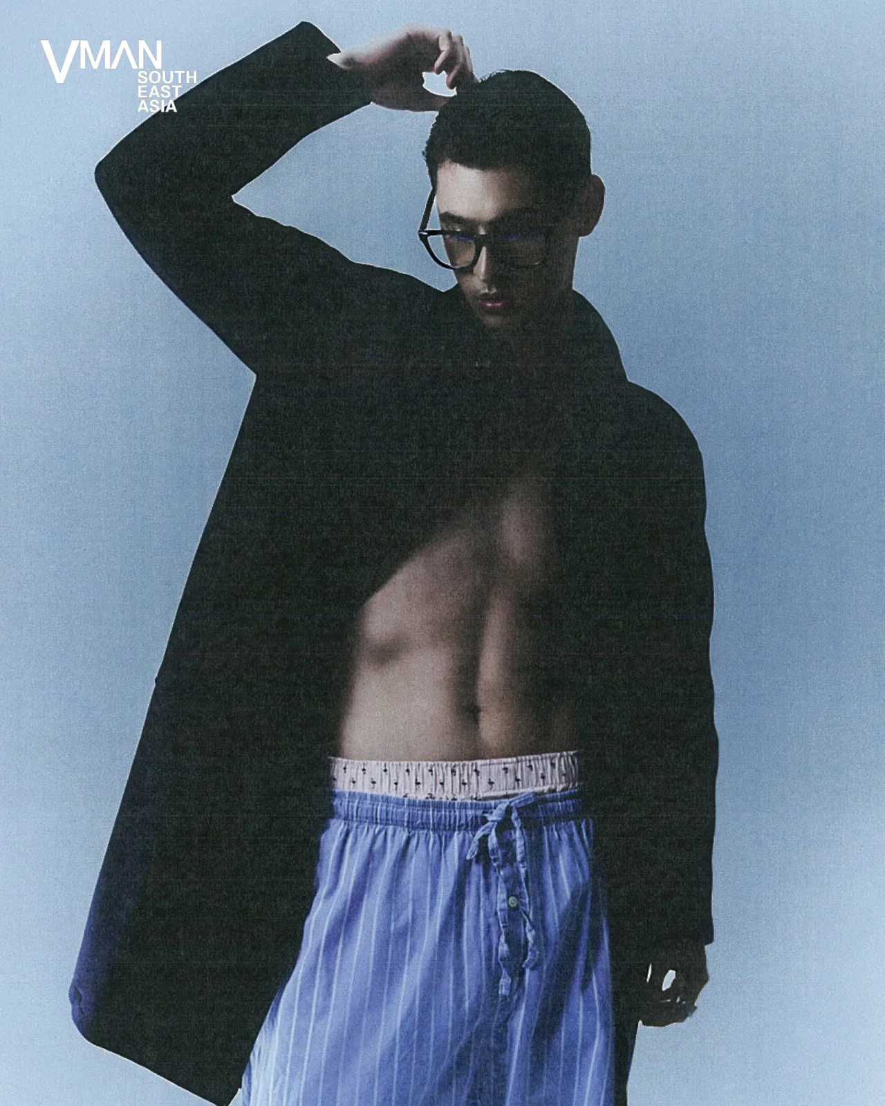 Model wearing an open black blazer over blue striped shorts against a pale blue background; logo 'VMAN South East Asia' in the top-left corner.