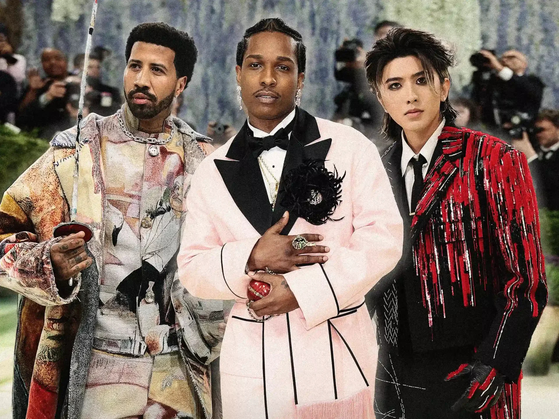 Three men posing on a fashion show red carpet in bold, embellished outfits; photographers in the background hold cameras.