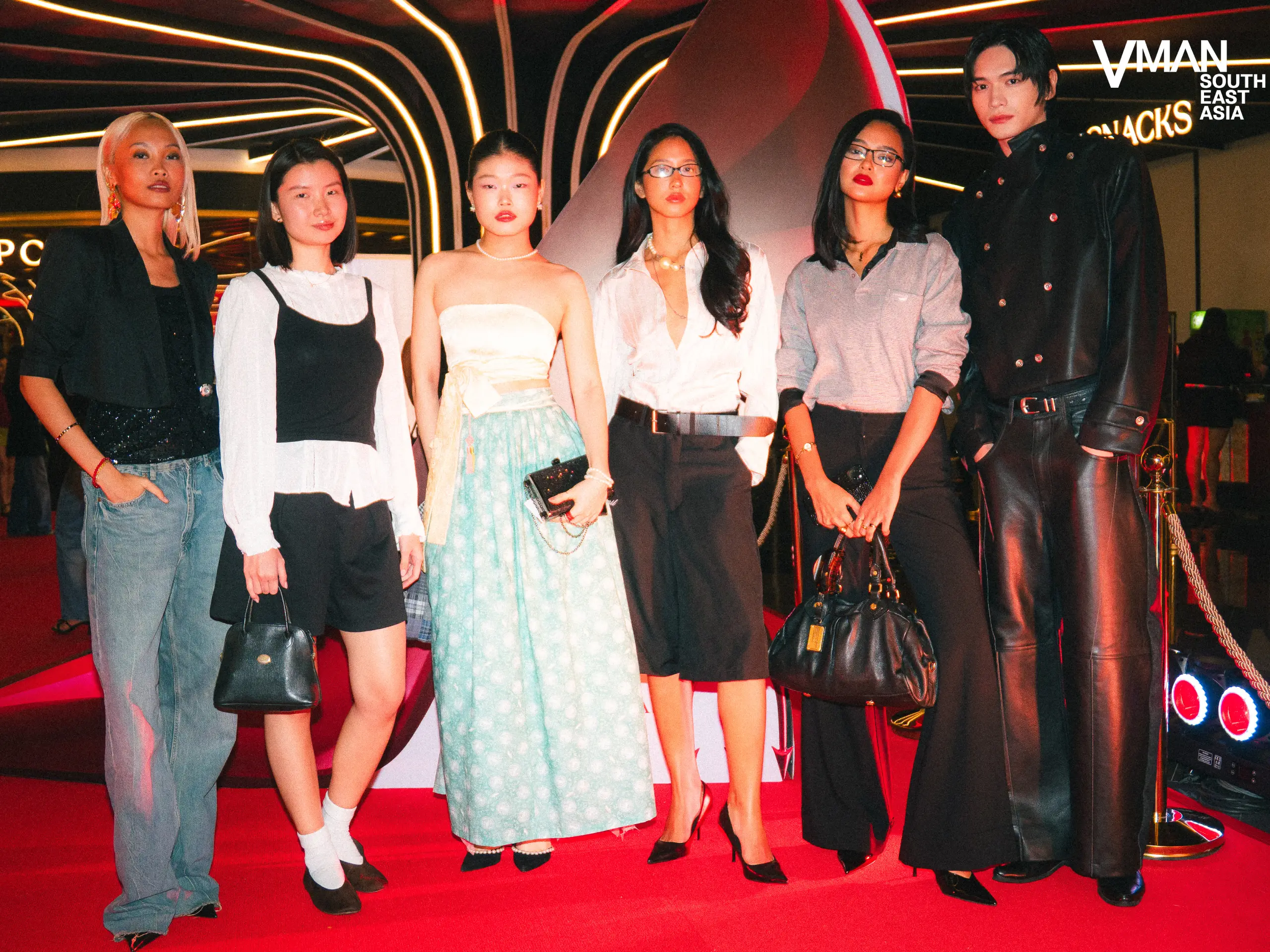 Six fashion models pose together on a red carpet at a neon-lit event, with the VMAN South East Asia logo visible in the top right.