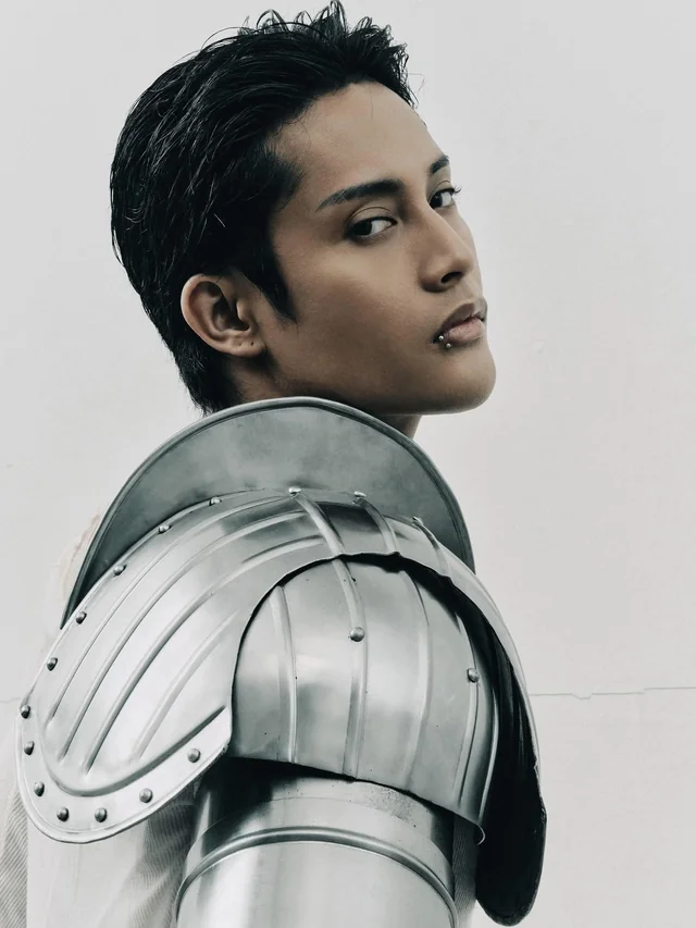 Young person wearing metallic knight armor shoulder pauldron, looking over their shoulder.