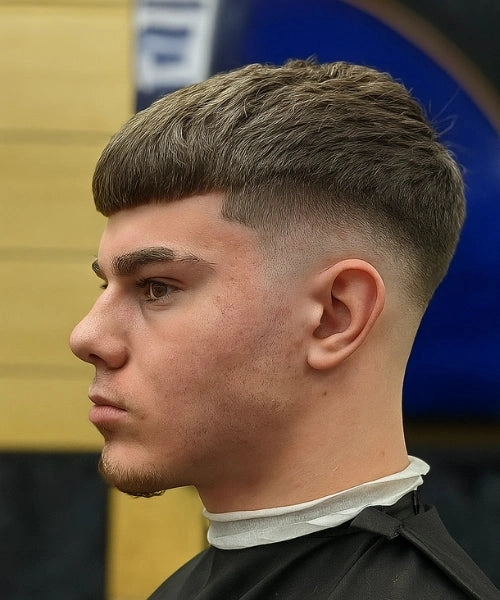 Side profile of a young man with a blunt fringe haircut and a high skin fade in a barber chair