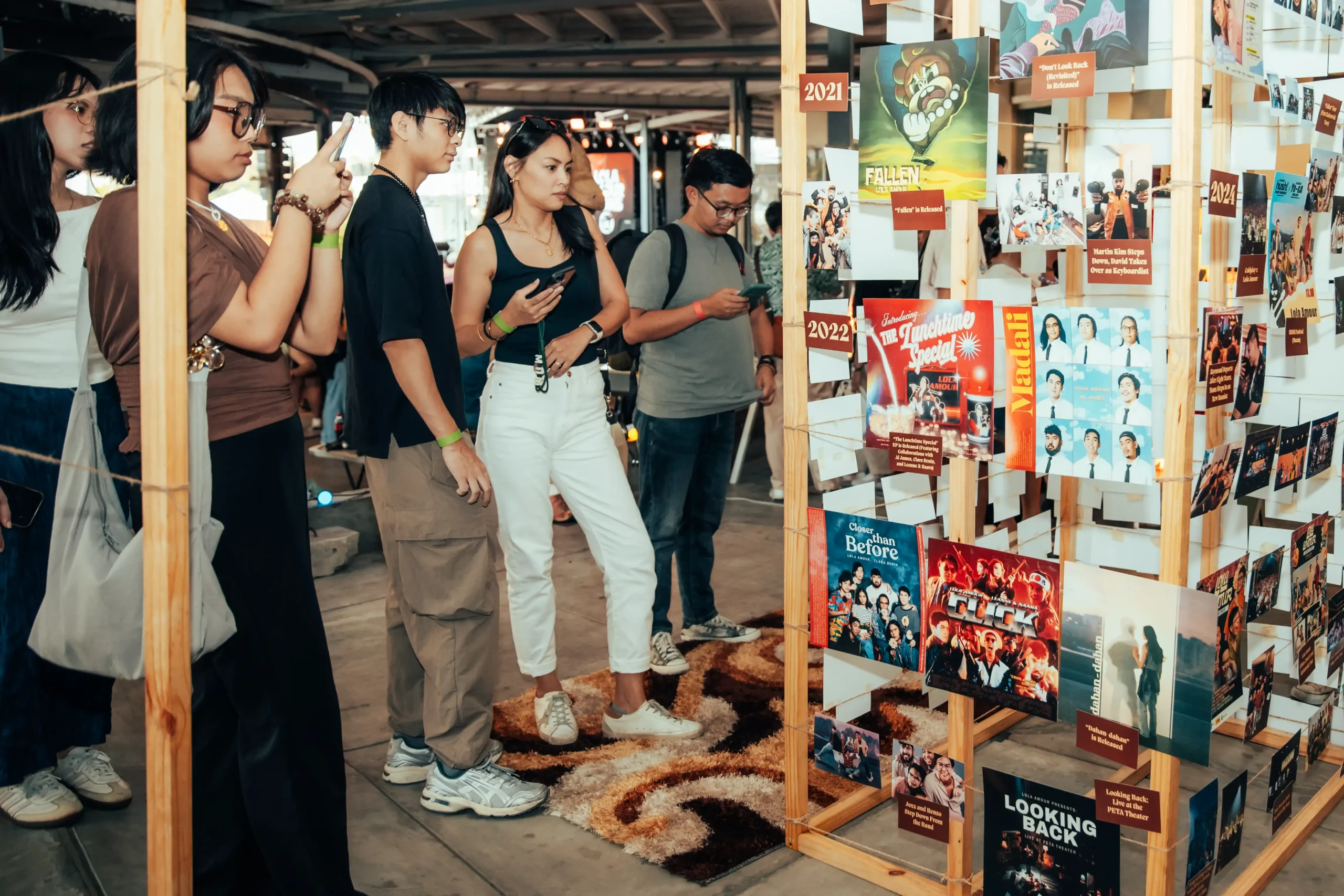 Group of people examining a wooden poster wall filled with colorful movie posters and photos.