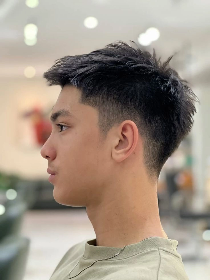 Side profile of a young man with a high fade and textured spiky top, indoors.